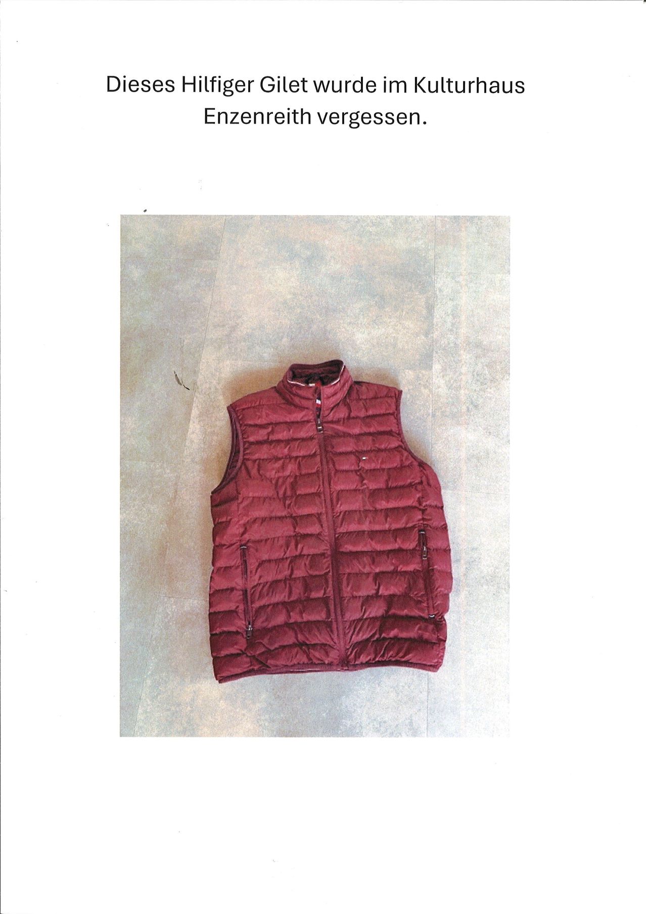 A maroon padded vest with a zipper is placed on a beige floor. It has a collar and zippered pockets.