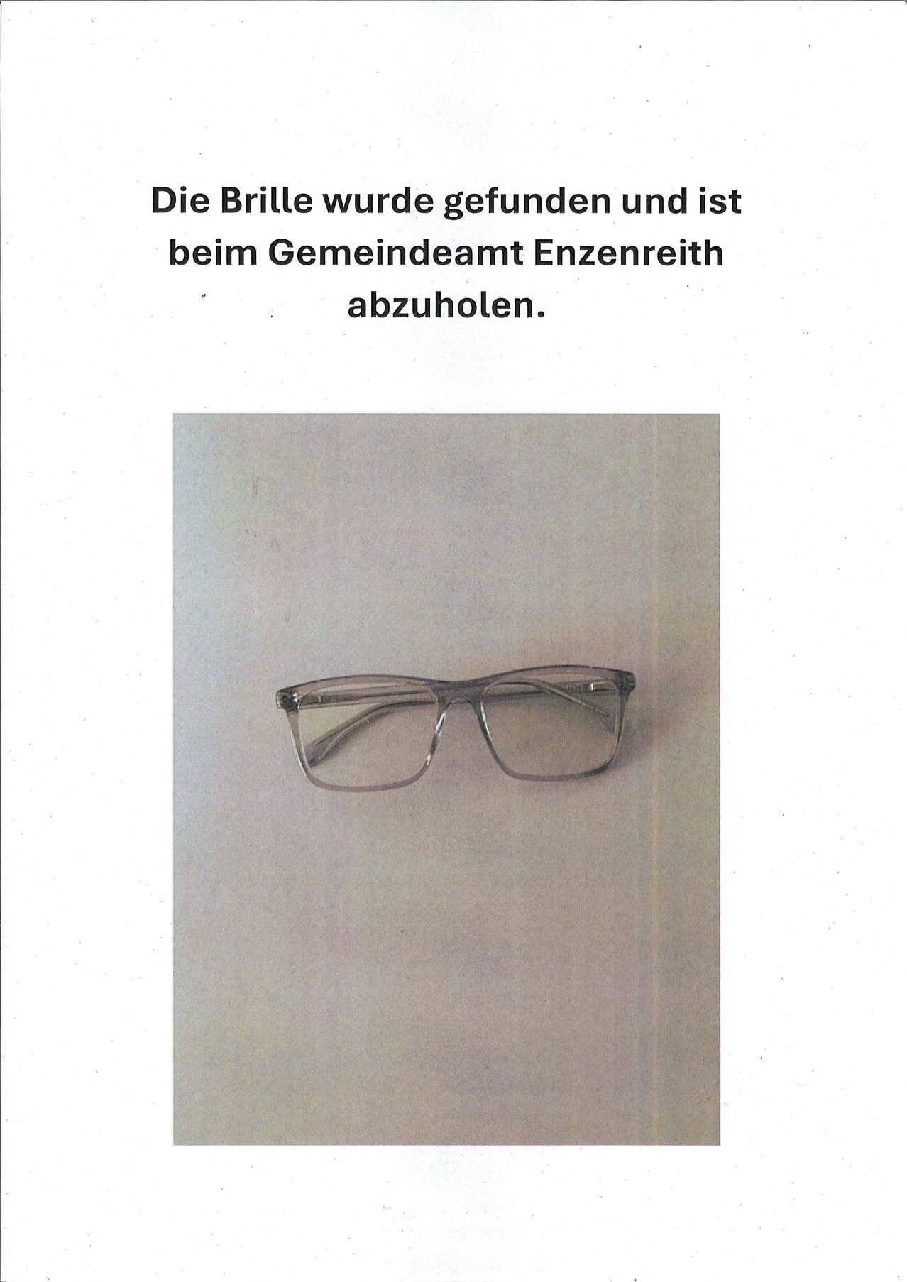 Ein Paar Brille mit klaren Rahmen wird auf einem hellgrauen Hintergrund gezeigt. Die Brille hat ein schlankes, modernes Design mit dünnen, silberfarbenen Rahmen.