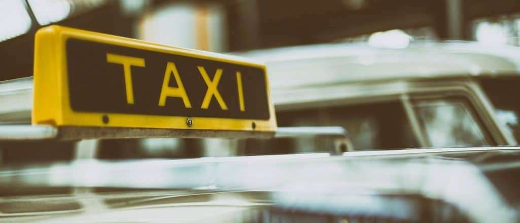 Ein gelbes Taxischild auf dem Dach eines Autos, das seine Verfügbarkeit anzeigt. Das Bild ist leicht unscharf.