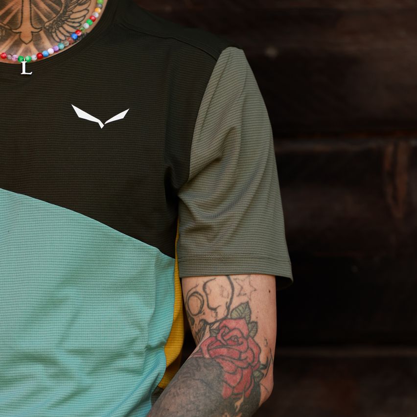 A person with tattoos on their arm and neck wearing a black and green sports shirt with a white bird logo.