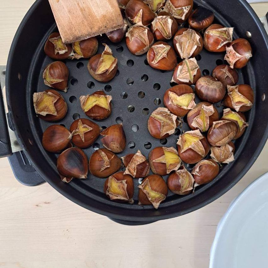 Eine Bratpfanne mit gerösteten Kastanien, mit einem hölzernen Kochlöffel an der Seite.