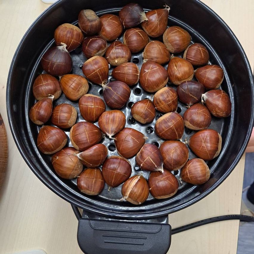 Ein schwarzer Airfryer-Korb gefüllt mit gerösteten Kastanien auf einer Holzoberfläche.