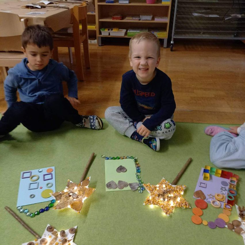 Zwei Jungen sitzen auf dem Boden, lächeln und sind von Kunstprojekten wie Sternen und bunten Formen umgeben.