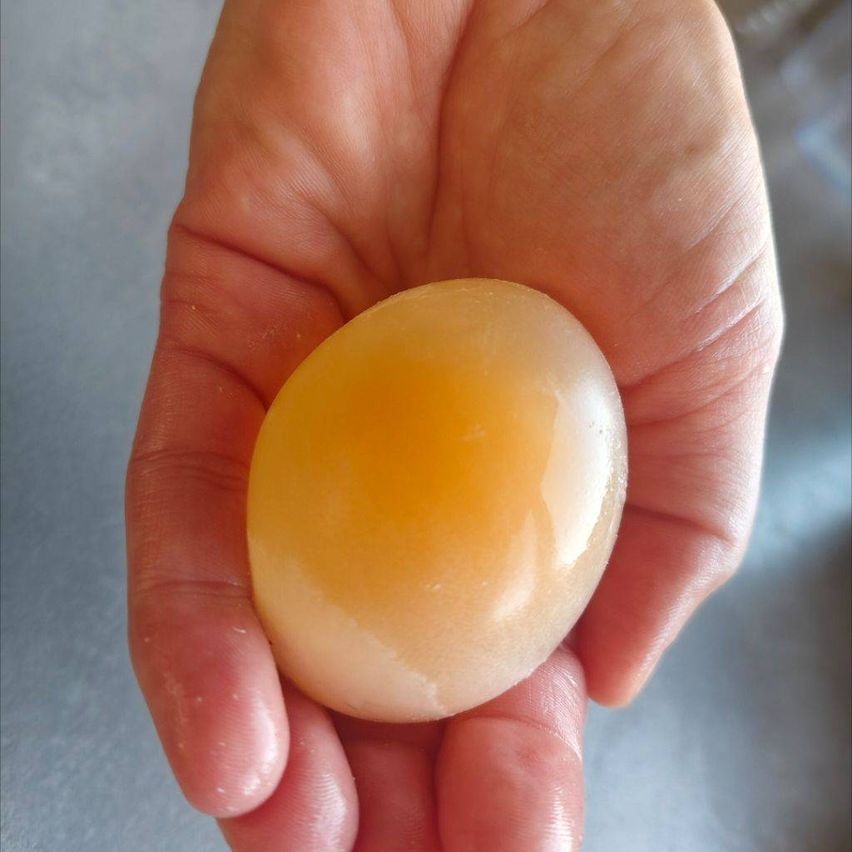 Eine Hand hält ein rundes, gelbes Eigelb, das Licht auf seiner Oberfläche reflektiert.