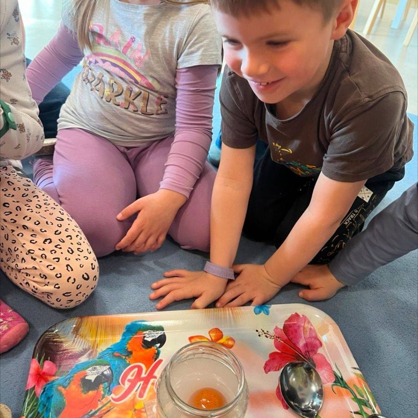Ein junger Junge greift nach einem Glas mit Eiern auf einem bunten Tablett, während ein Mädchen in der Nähe sitzt. Beide tragen Freizeitkleidung.