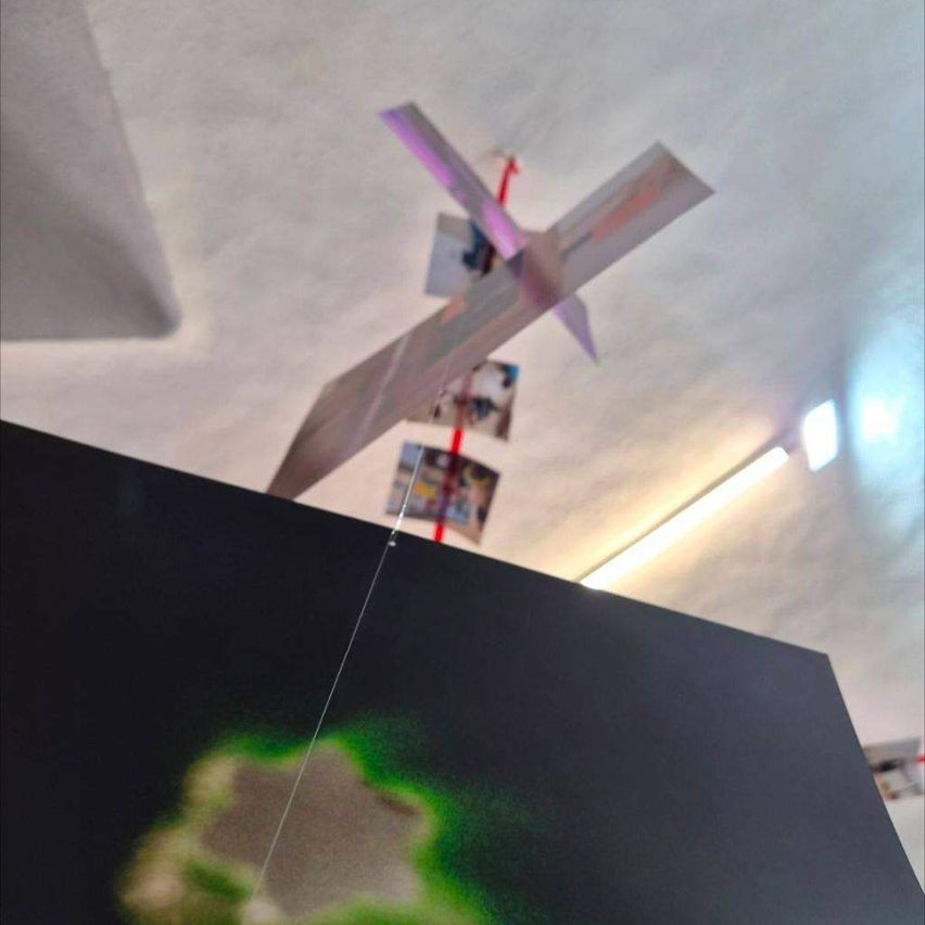 Ein schwarzes Objekt mit grüner Lichtanzeige steht auf einem Tisch. Papierflugzeuge hängen von der Decke. Eine Lampe ist an der Wand.
