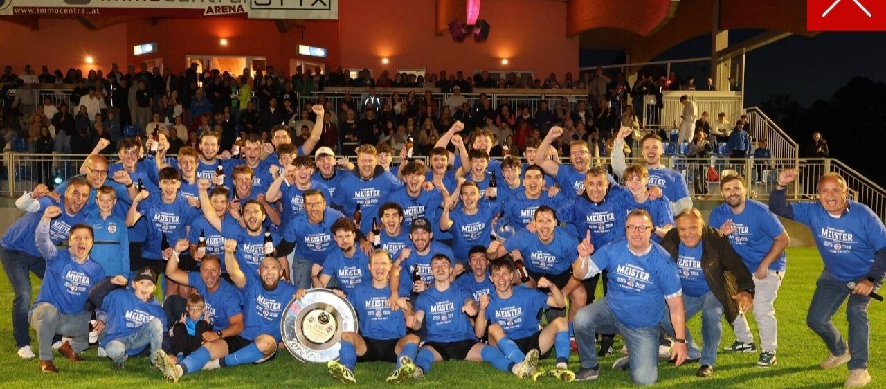 Eine Fußballmannschaft feiert mit einer Trophäe auf einem Feld, umgeben von Fans in einem Stadion. Die Spieler tragen blaue Trikots mit 'Meister' darauf.