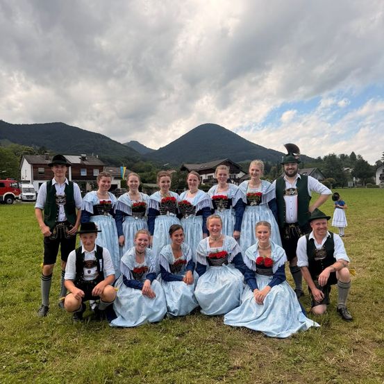 Eine Gruppe von Menschen in traditioneller Kleidung posiert für ein Foto auf einer Wiese mit Bergen im Hintergrund.