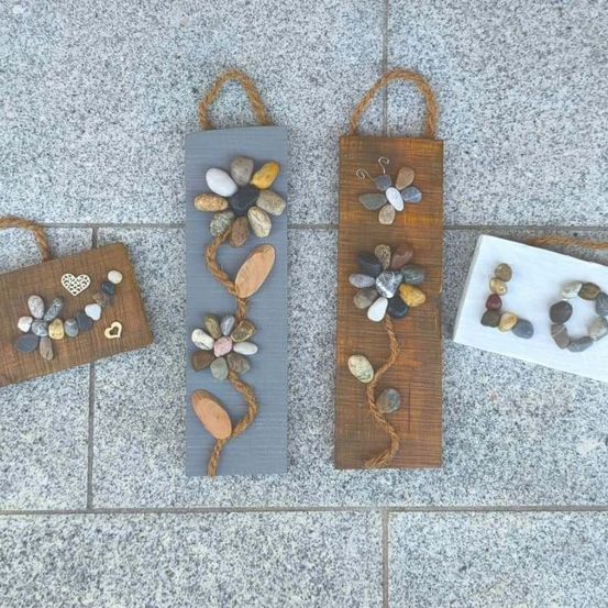 Vier handgefertigte Dekorationen aus Steinen, Blumen und Herzen. Drei sind an Brettern befestigt und eine ist ein kleiner Beutel.