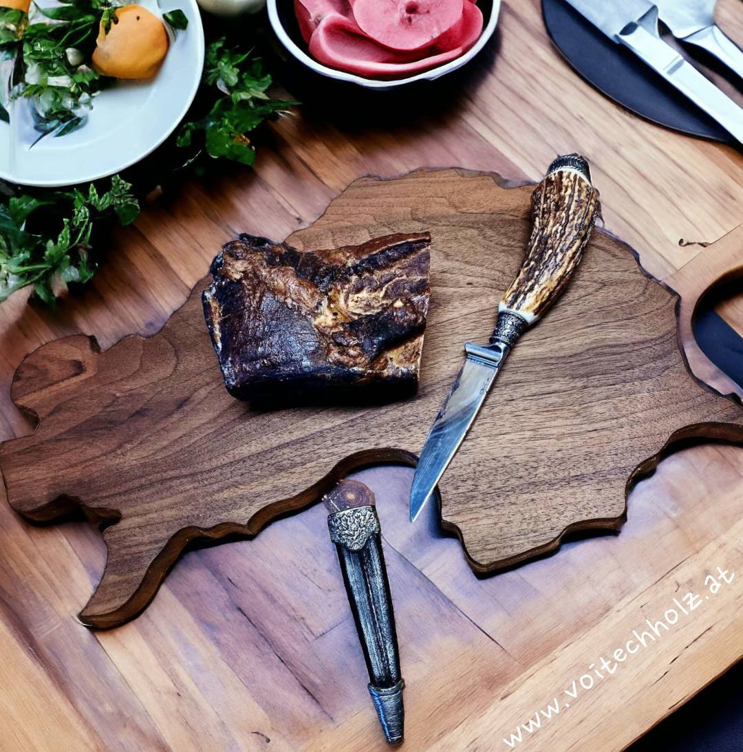 Ein holzernes Schneidebrett in Form eines Landes, mit einem Stück Fleisch, einem Messer und einer Gabel darauf.