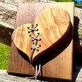 Ein holzherz mit gesticktem design liegt auf einem holzbrett, das auf einem holzzaun ruht. das herz ist aus holz gefertigt und weist ein kreuzstichmuster auf.