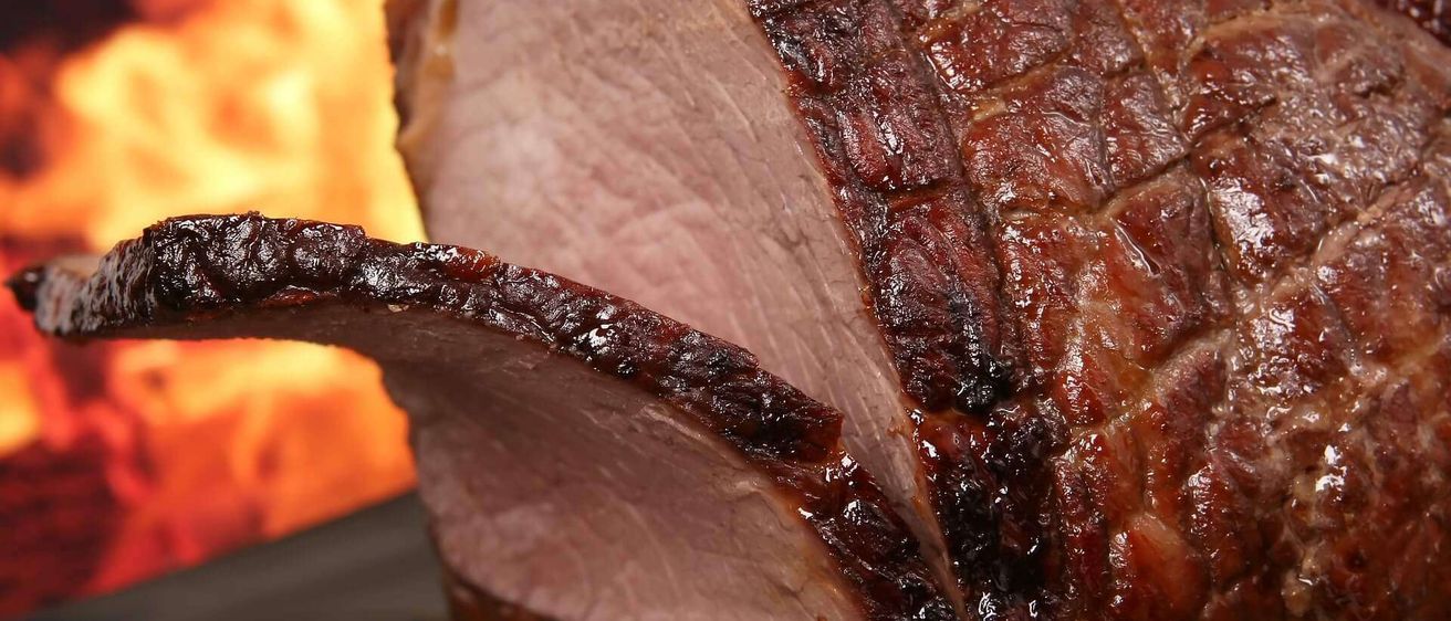 Ein Nahaufnahme eines gebratenen Schweinelende mit knuspriger, karamellisiert Kruste, vor einem Hintergrund von brennenden Flammen dargestellt.