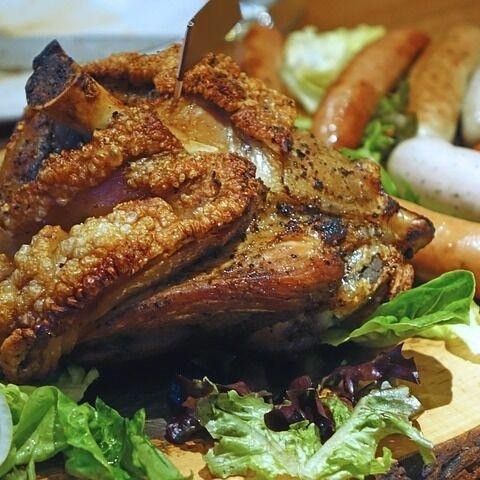 Ein Nahaufnahme von einem gebratenen Fleischgericht, knusprig außen, mit grünem Salat garniert. Würste sind daneben.