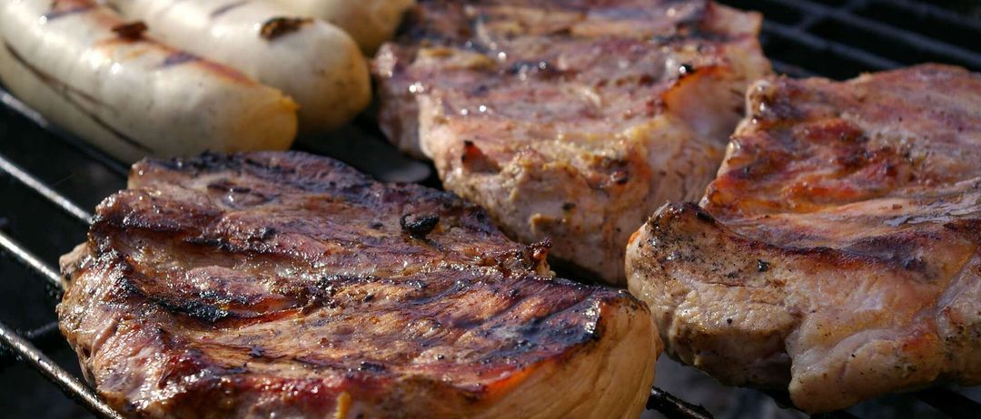 Ein Nahaufnahme von gegrillten Fleischsorten, einschließlich Würsten, auf einem Grill. Das Fleisch ist verkohlt mit einigen schwarzen Flecken.