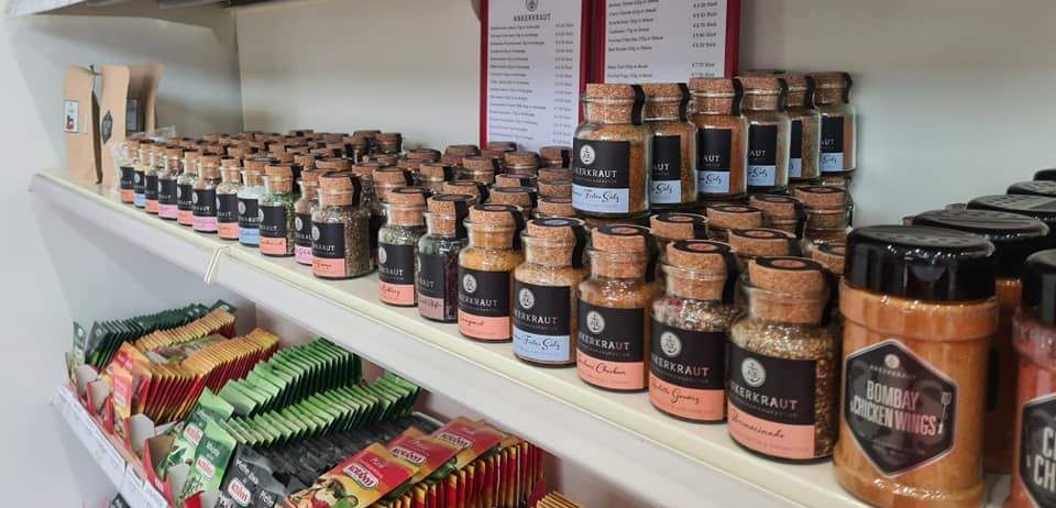 Ein Regal gefüllt mit verschiedenen Gewürzen und Tees, einschließlich etikettierter Gläser und Packungen mit unterschiedlichen Geschmacksrichtungen und Marken.