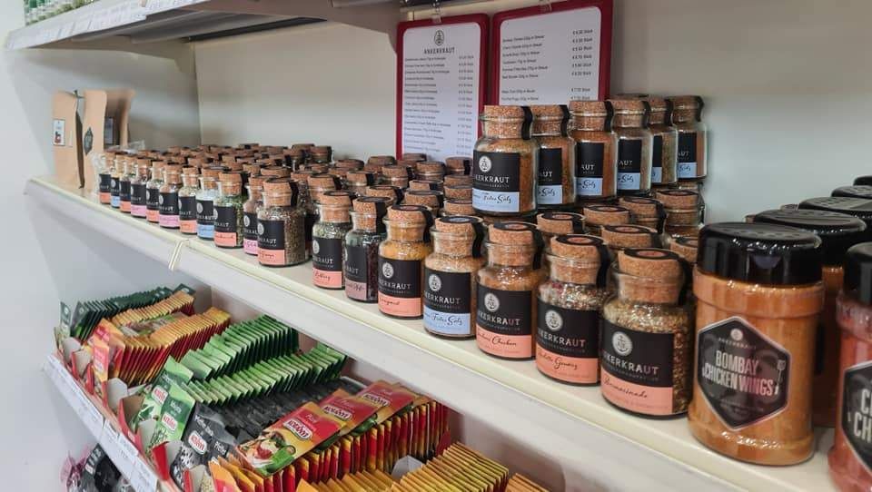 Ein Regal gefüllt mit verschiedenen Gewürzen und Tees, einschließlich etikettierter Gläser und Packungen mit unterschiedlichen Geschmacksrichtungen und Marken.