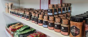 Ein Regal gefüllt mit verschiedenen Gewürzen und Tees, einschließlich etikettierter Gläser und Packungen mit unterschiedlichen Geschmacksrichtungen und Marken.