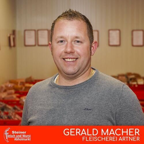 Ein Mann steht lächelnd in einem Geschäft. Er trägt ein graues Sweatshirt und eine Halskette. Hinter ihm ist eine rote Aufbewahrungsbox zu sehen. Darüber hängen mehrere gerahmte Urkunden an der Wand. Das Bild hat einen roten Rand und Textüberlagerung.