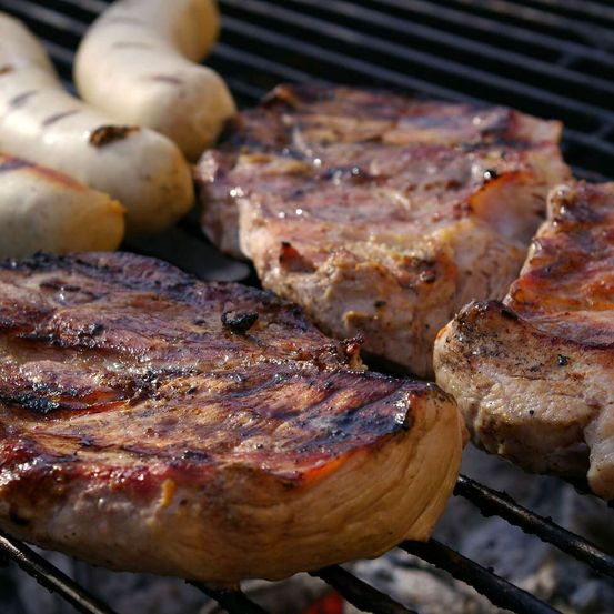 Ein Nahaufnahme von gegrilltem Fleisch auf einem Grill, einschließlich Würste und Steaks mit Grillspuren und Säften.