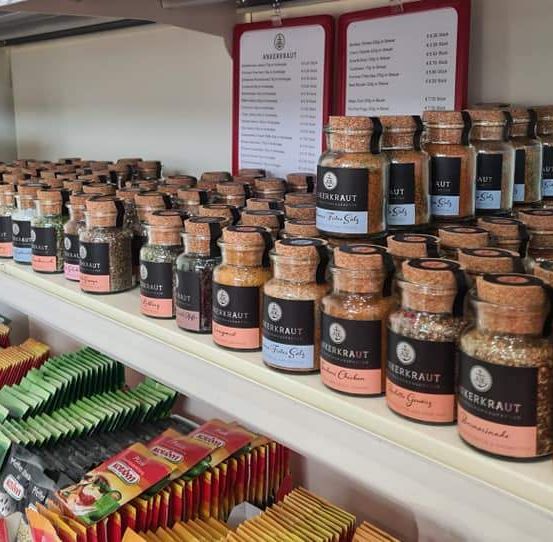 Ein weißer Regalboden zeigt eine Vielzahl kleiner Flaschen und Gläser. Die Flaschen sind mit verschiedenen Gewürzen beschriftet. Es gibt auch einige Schachteln mit Teebeuteln und anderen Artikeln auf dem Regal.