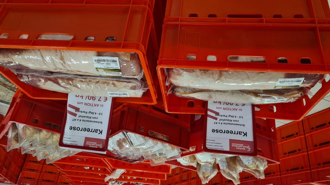 Rote Kisten mit verpackten Fleischprodukten und roten Etiketten, die 'Kelbasa' lesen. Die Fleischprodukte sind in Plastik eingewickelt und auf Regalen platziert.