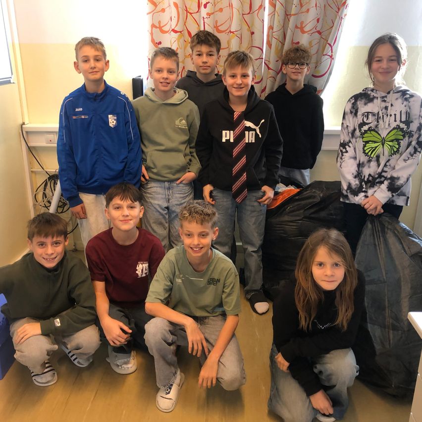 Eine Gruppe junger Jungen und Mädchen posiert für ein Foto mit einigen Müllsäcken in einem Raum. Sie lächeln und scheinen glücklich zu sein.