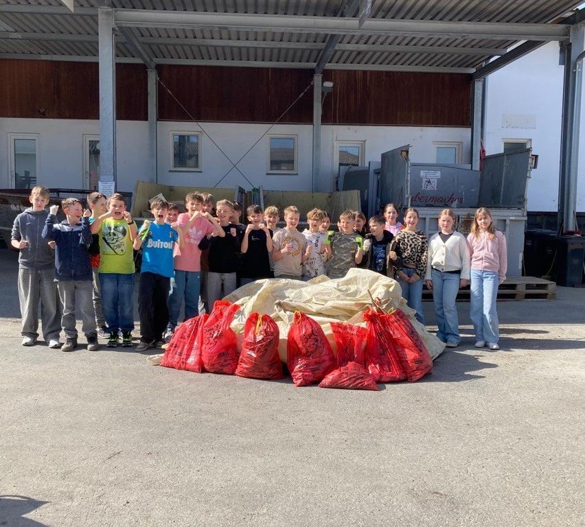 Group of kids and young adults standing around a pile of red bags in front of a building with a shed.