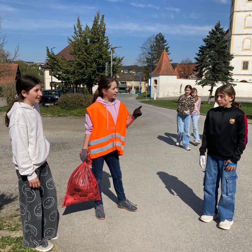 A group of young girls are standing on a road with a building in the background. One of them is holding a red garbage bag.