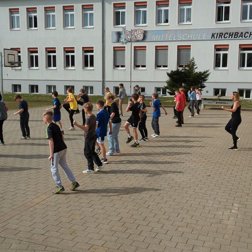 Schüler machen Übungen vor der Mittelschule Kirchbach. Eine Frau geht hinter ihnen her.