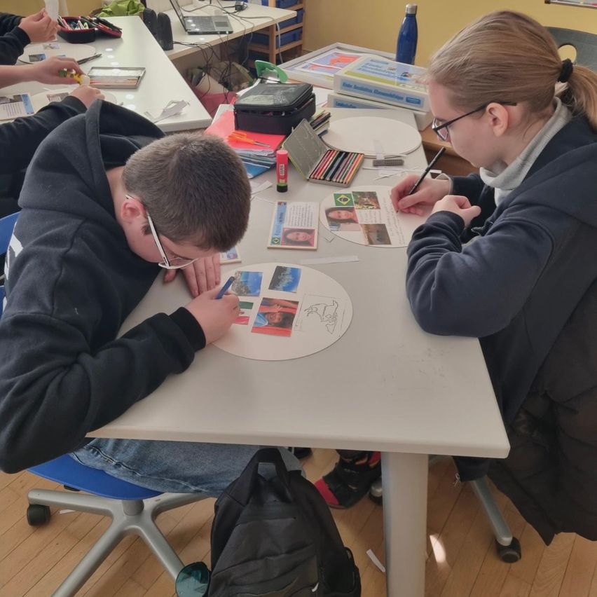 Ein Junge und ein Mädchen sitzen an einem Tisch. Sie arbeiten an einem Projekt mit Fotos, Aufklebern und anderen Materialien.