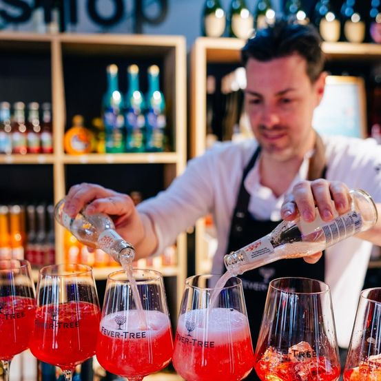 Ein Barkeeper gießt einen roten Cocktail in Gläser in einer Bar. Der Cocktail ist mit Fever-Tree gekennzeichnet.