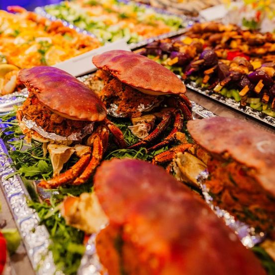 Eine Nahaufnahme von Krabbengerichten auf einem Buffettisch, mit gefüllten Krabben und Garnierungen, umgeben von anderen Meeresfrüchten und Gemüsegerichten.