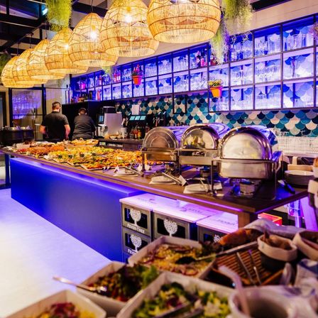 Ein Restaurantbuffet mit einer Vielzahl von Gerichten, blauer Beleuchtung und dekorativen Hängelampen.
