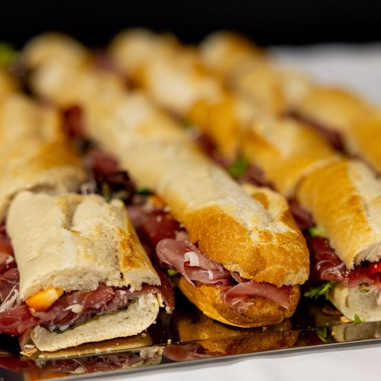 Eine Nahaufnahme verschiedener Sandwiches auf einem Tablett, einschließlich eines Sandwiches mit geschnittenem Fleisch, Gemüse und Käse.