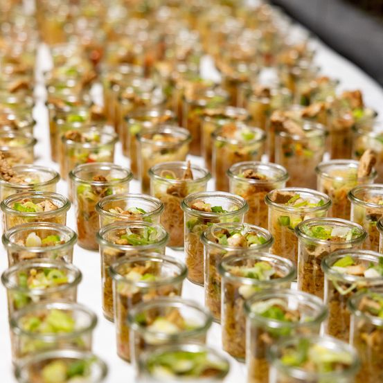 Viele Glasgläser mit verschiedenen Lebensmitteln, einschließlich Gemüse, Fleisch und Saucen, sind auf einer weißen Oberfläche angeordnet.