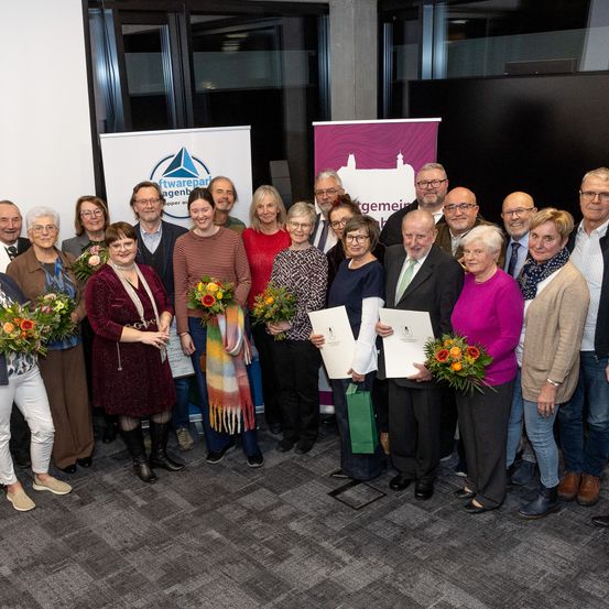 Eine Gruppe von Menschen posiert für ein Foto mit Blumen und Urkunden in einem Raum mit Bannern an der Wand.
