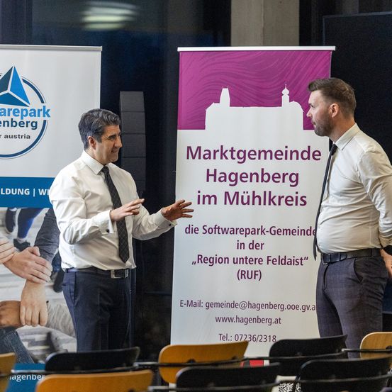 Zwei Männer in formeller Kleidung stehen vor einem Banner für einen Softwarepark in Hagenberg, Österreich.