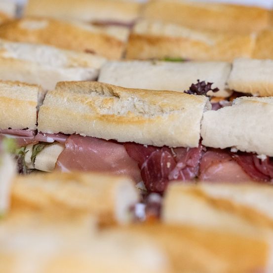 Eine Nahaufnahme von mehreren Sandwiches mit Fleischscheiben und Salat auf Weißbrot.
