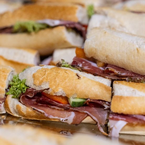 Eine Nahaufnahme mehrerer Sandwiches auf einem Tablett, mit Fleischscheiben, Salat und Tomaten, einige mit Gurkenscheiben.