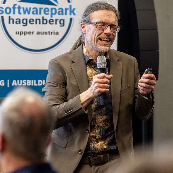 Ein Mann in einem Anzug spricht in ein Mikrofon auf einer Konferenz in Hagenberg, Oberösterreich.