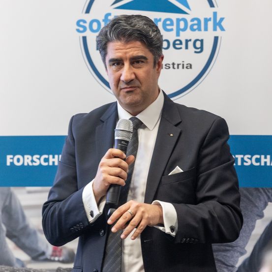 Ein Mann spricht in ein Mikrofon vor einem Schild mit der Aufschrift 'Forschungszentrum' und 'sofreparkberg'.