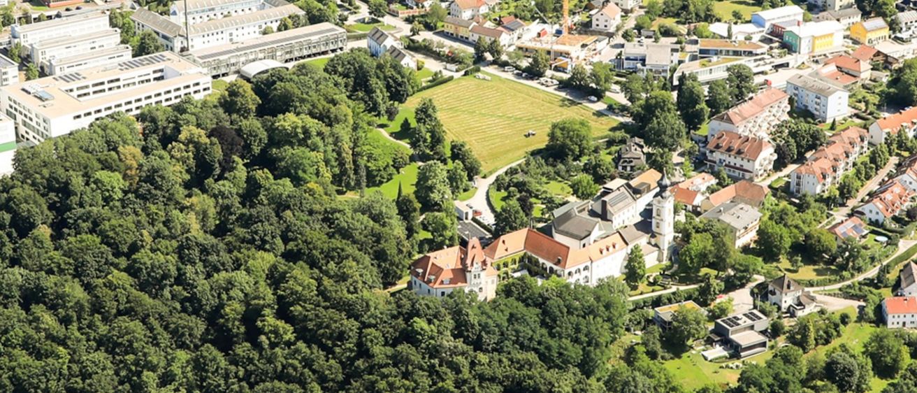 Ein Luftbild einer Stadt umgeben von üppigen grünen Bäumen, Gebäuden und Ackerland unter einem klaren Himmel.