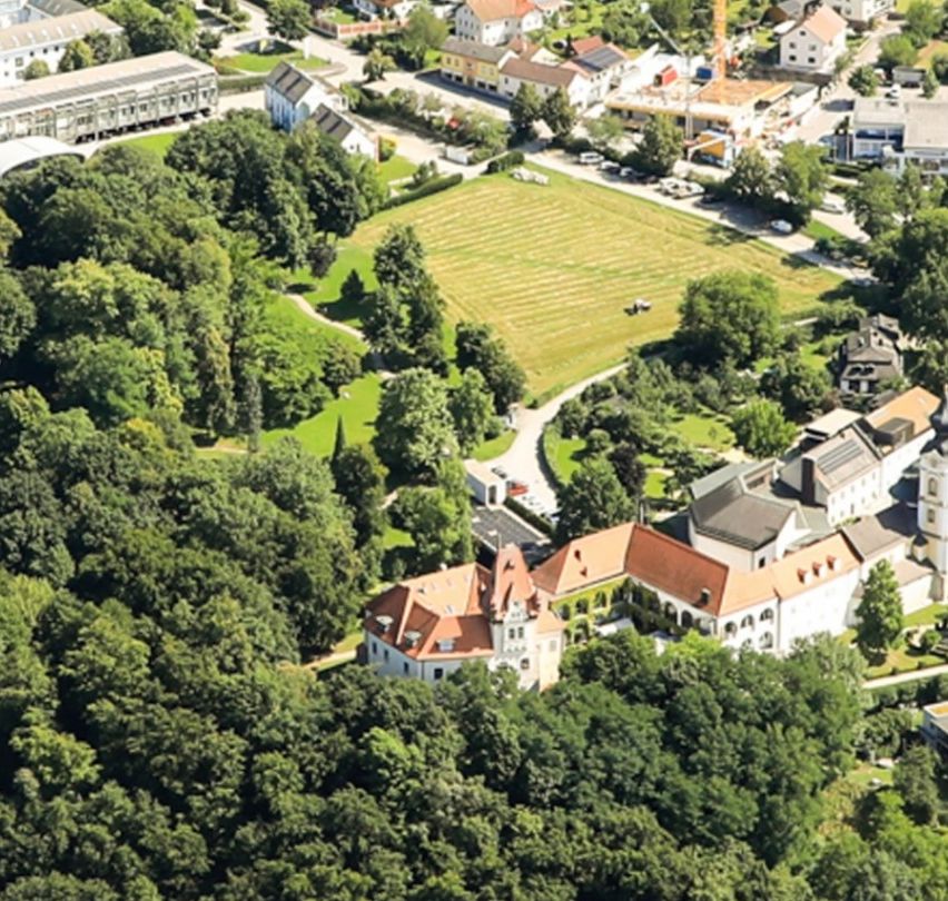 Ein Luftbild einer Stadt umgeben von üppigen grünen Bäumen, Gebäuden und Ackerland unter einem klaren Himmel.