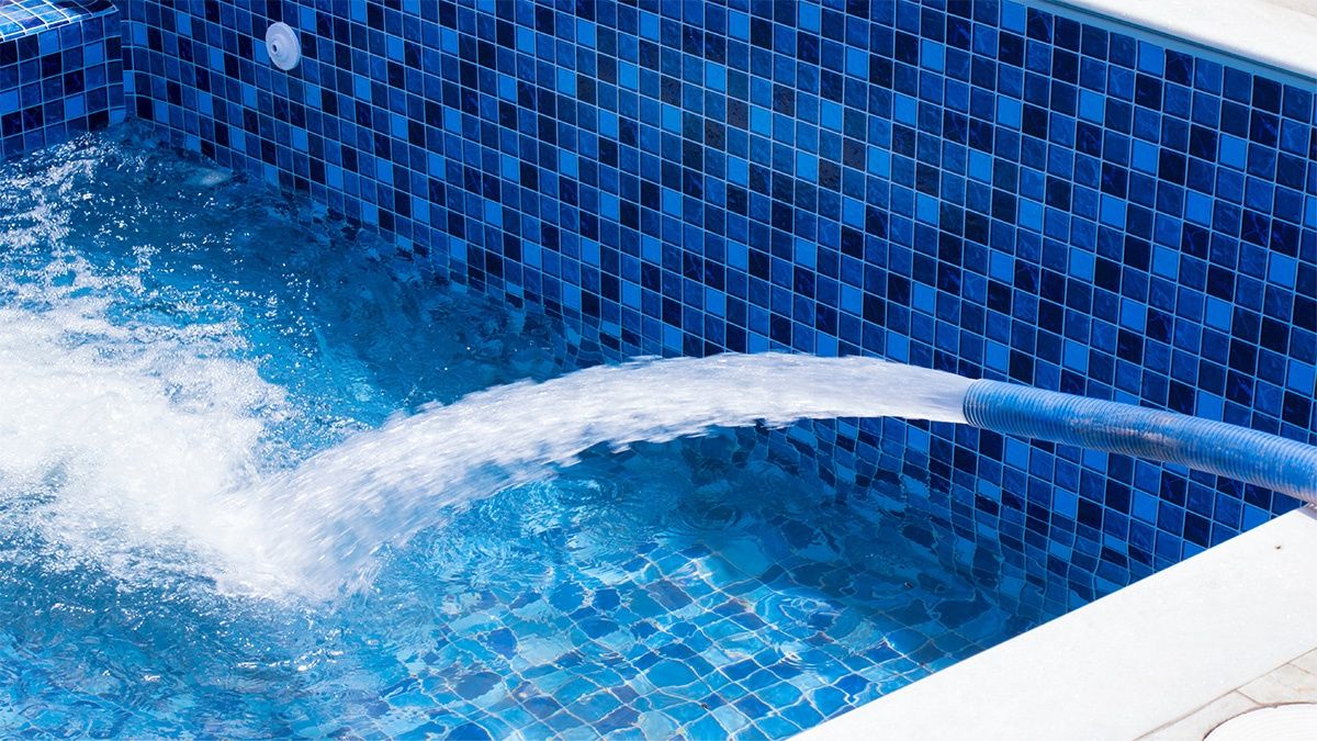 A pool filled with clear blue water and blue tiled walls with a hose pouring water into it.