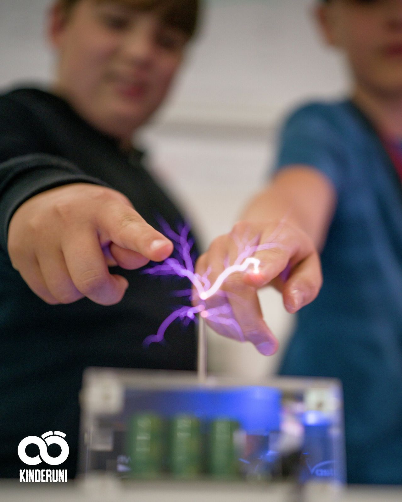 Two people are demonstrating a spark of electricity between their fingers, powered by a battery.