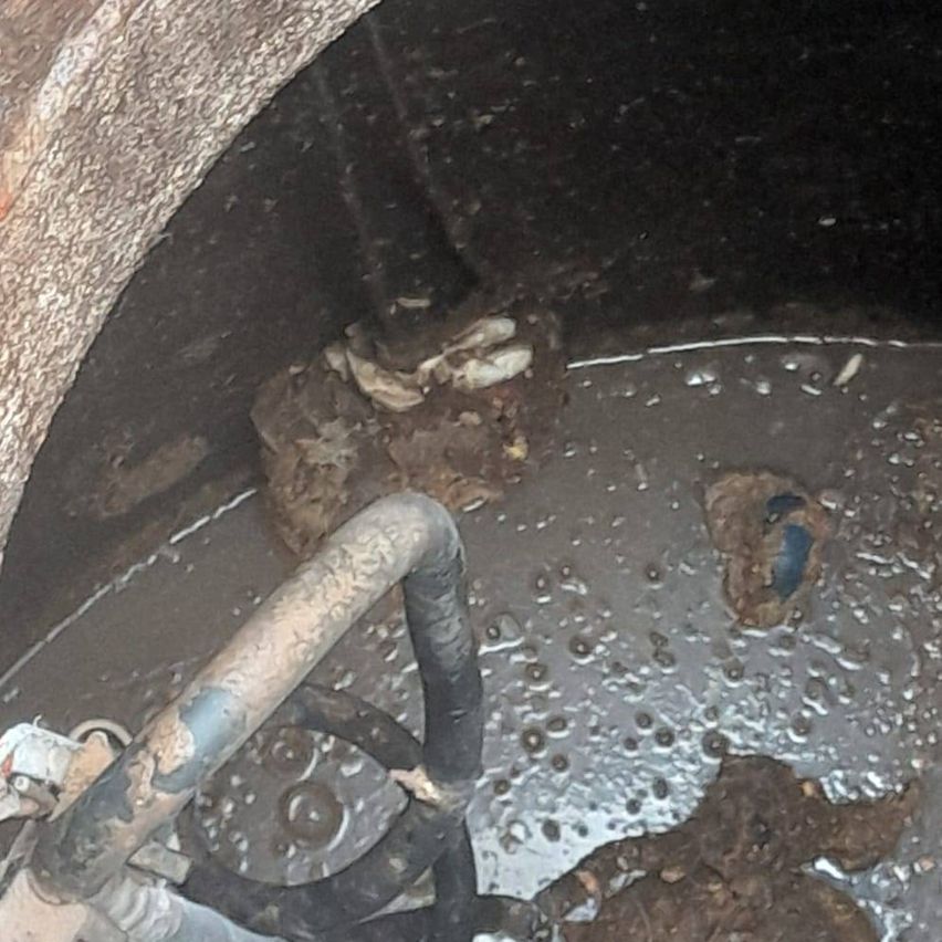 Eine Nahaufnahme eines dunklen, schmutzigen Abwasserkanals mit Rohren und Trümmern in trübem Wasser. Ein rostige Rohr ist sichtbar.