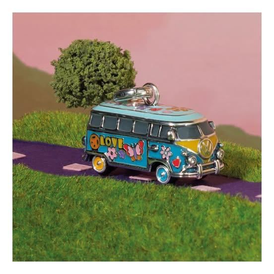 Ein farbenfrohes Modell eines alten VW-Busses mit einem Anhänger, geparkt auf einem grünen Rasen mit einem rosa Hintergrund.