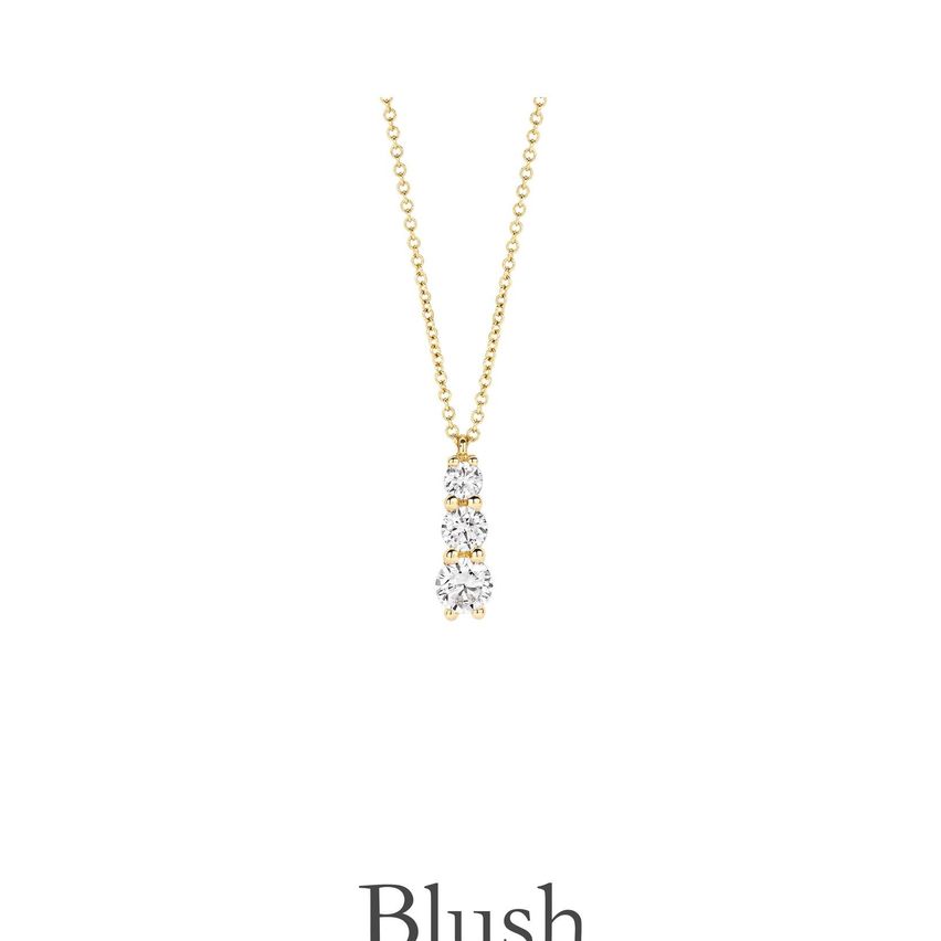 Eine goldene Halskette mit einem Anhänger, der drei Diamanten aufweist. Unten steht das Wort Blush.