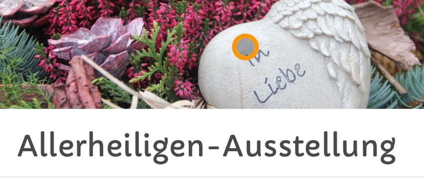 Ein herzförmiger Stein mit Engelsflügeln und dem Wort 'In Liebe' darauf steht zwischen rosa Blumen. Unten steht ein Text 'Allerheiligen-Ausstellung' mit einem Datumsbereich vom 17.10. bis 31.10.2025.