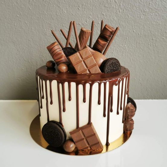 Ein Schokoladenkuchen mit weißer Glasur, Schokoladensauce und verschiedenen Schokoladen und Keksen darauf.